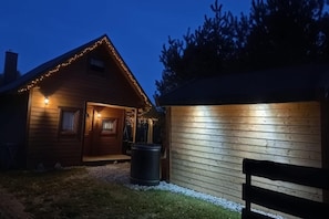 A wooden cabin with a porch and string lights, a trash bin, and a bench. - Holiday home, private sauna and jacuzzi (Balachy)