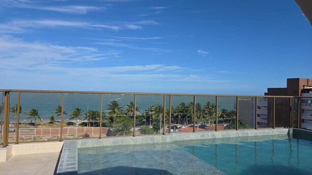 Une piscine offrant une vue dégagée sur l’oc éan et les palmiers, entourée d’une rambarde en verre.