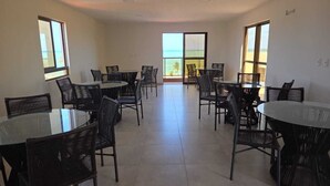 Un vaste espace dédié à la salle à manger, avec plusieurs tables et chaises rondes, de grandes fenêtres offrant une vue sur la plage et un intérieur lumineux et bien éclairé.