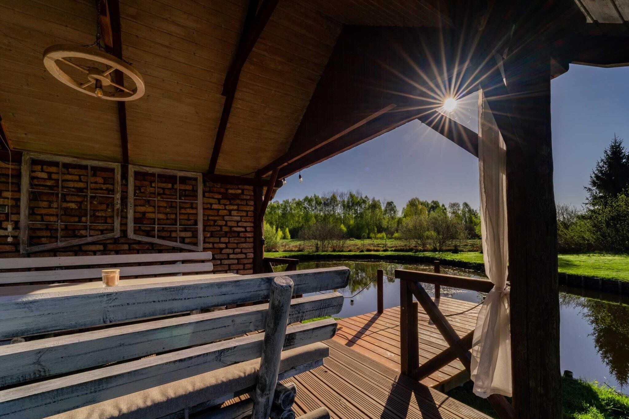 A wooden deck with a bench and a table, overlooking a calm body of water and a grassy landscape.