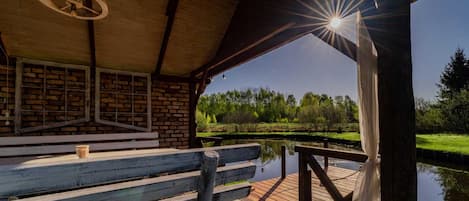 A wooden deck with a bench and a table, overlooking a calm body of water and a grassy landscape.