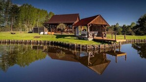 Uma cabana de madeira com um cais, rodeada por um lago calmo e árvores.