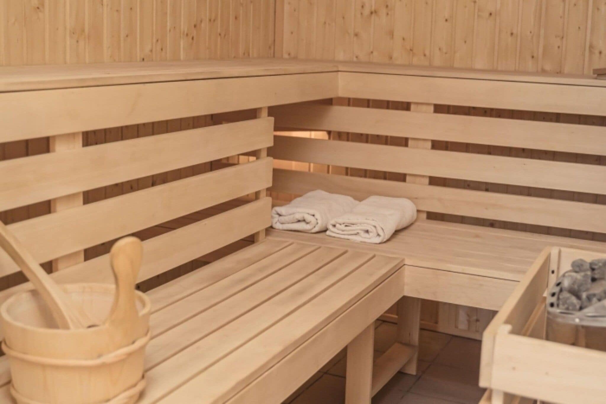 Eine Saunabank aus Holz mit Handtüchern, einem Holz-Eimer und einem Behälter mit Steinen.