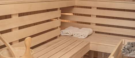 Um banco de sauna de madeira com toalhas, um balde de madeira e um recipiente com pedras.