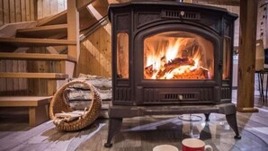 Una habitación acogedora con un estufa de leña, una cesta tejida y dos tazas sobre una mesa de vidrio.