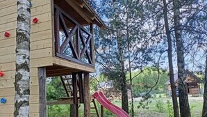 Una casita de madera con un tobogán rojo, rodeada de árboles y una piscina infantil azul.