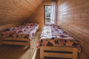 Eine Holzhütte mit zwei Etagenbetten, einer geneigten Decke und einem Fenster mit Blick ins Freie.