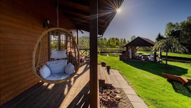 Una terraza de madera con una hamaca colgante, un área de estar al aire libre techada y un jardín con césped.