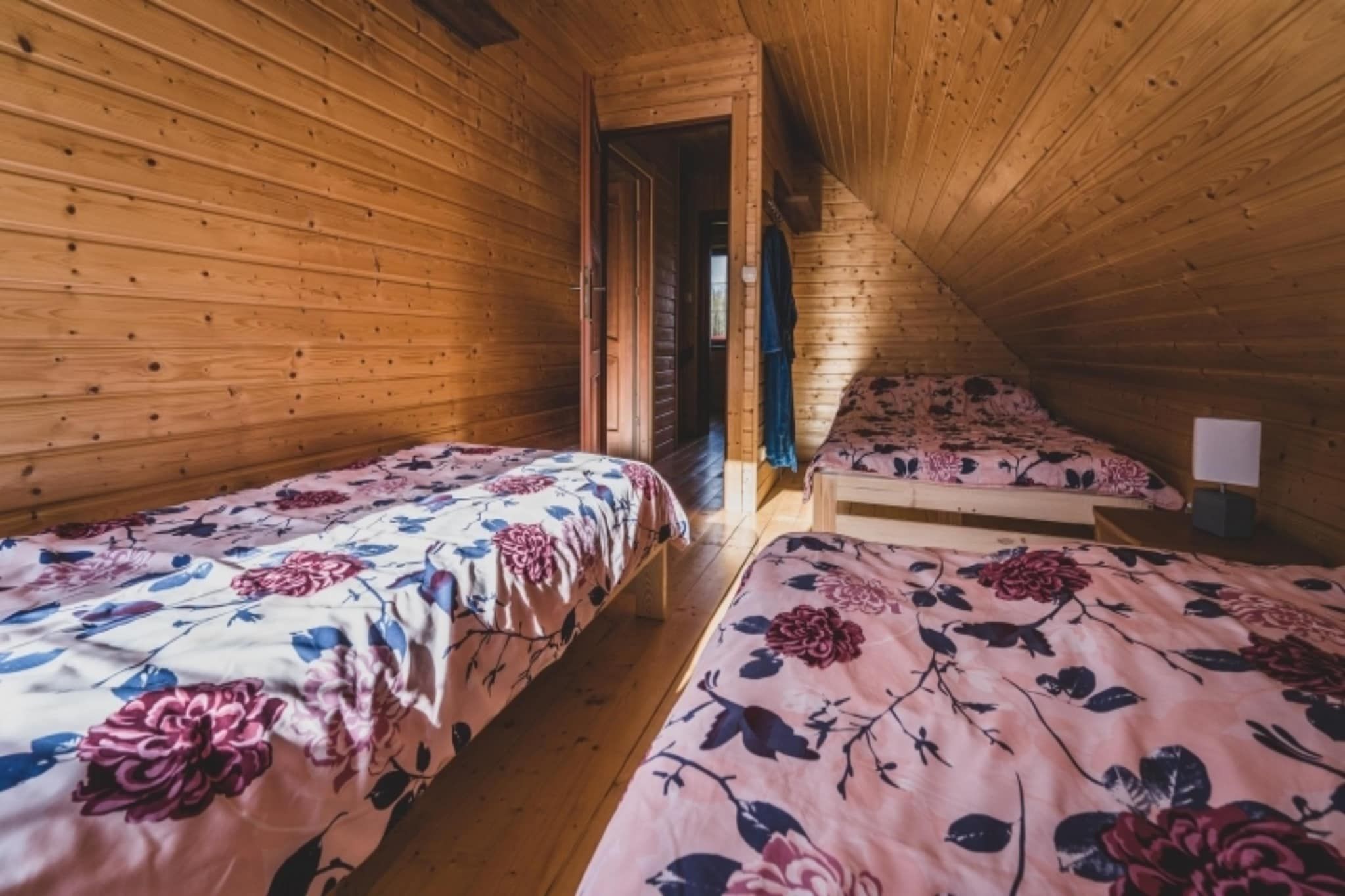 A wooden cabin with two single beds, each with floral bedding, and a small table with a lamp.