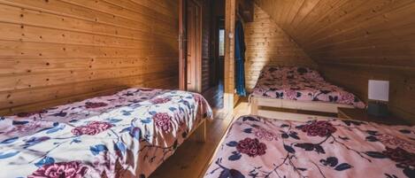 A wooden cabin with two single beds, each with floral bedding, and a small table with a lamp.