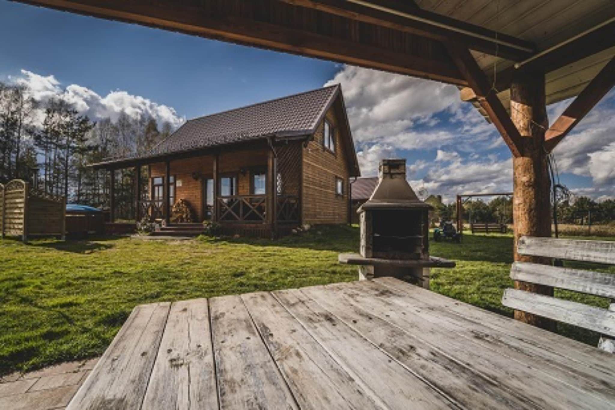 A wooden cabin with a porch, a barbecue grill, and a grassy yard.