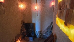 A stone-walled interior with a wooden bench, a stone wall with a yellow-lit section, and a small rock formation.