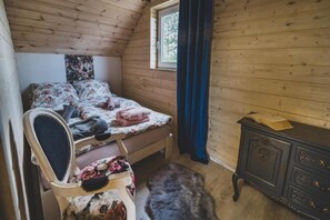 A bedroom with a wooden ceiling, a bed with floral bedding, a chair with a floral cushion, a dresser, and a window with a curtain. - Large holiday home, jacuzzi, sauna, salt cave (Balachy)