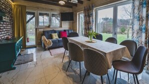 A dining area with a table and chairs, a sofa with cushions, a television on the wall, and a view of the outdoors through large windows. - Large holiday home, salt cave, jacuzzi, sauna (Balachy)