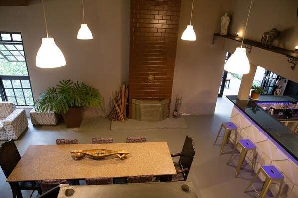 A modern interior with a central brick wall, hanging pendant lights, a wooden table with a decorative bowl, and a bar area with stools.