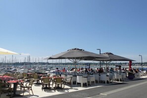 An outdoor dining area with tables and chairs, umbrellas, and a view of the marina in the background. - Terraced Country House near Sea (Plurien)