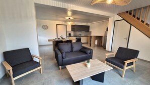 Ein modernes Wohnzimmer mit einer Couch, zwei Sesseln, einem Couchtisch und einer Küche im Hintergrund.