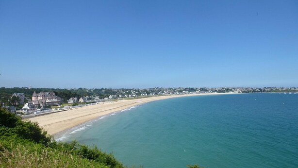 Blick auf die Küste mit einem Sandstrand, wolkenlosem, blauem Himmel und einer Reihe von Häusern am Ufer.
