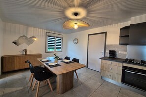 A modern kitchen with a dining area, wooden cabinets, and a unique ceiling light fixture. - Terraced Country House near Sea (Plurien)