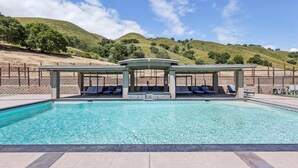 Una piscina con lettini e un'area relax coperta, immersa in un paesaggio collinare.