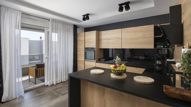 A modern kitchen with wooden cabinets, a black countertop, and a fruit bowl. - Luxury Penthouse Pula (Pula)