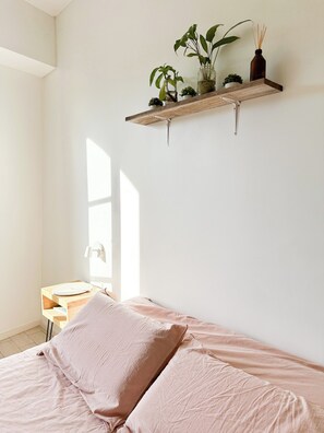 A bedroom with a bed, a bedside table, a small desk, and a shelf with plants. - Cozy studio apartment in marvelous Palermo, Arcos District with AC and balcony (Buenos Aires)