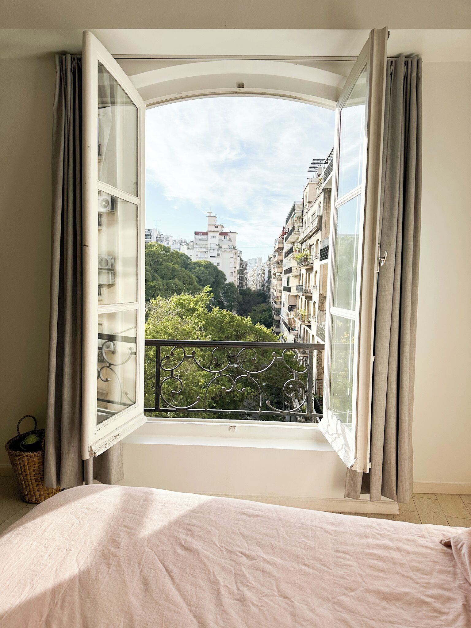 A bedroom with an open window revealing a cityscape and greenery.