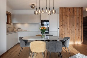 A modern kitchen with a central island, grey chairs, and a wooden accent wall. - Taiga – Central Apartment Near Slopes, Huez (Huez)