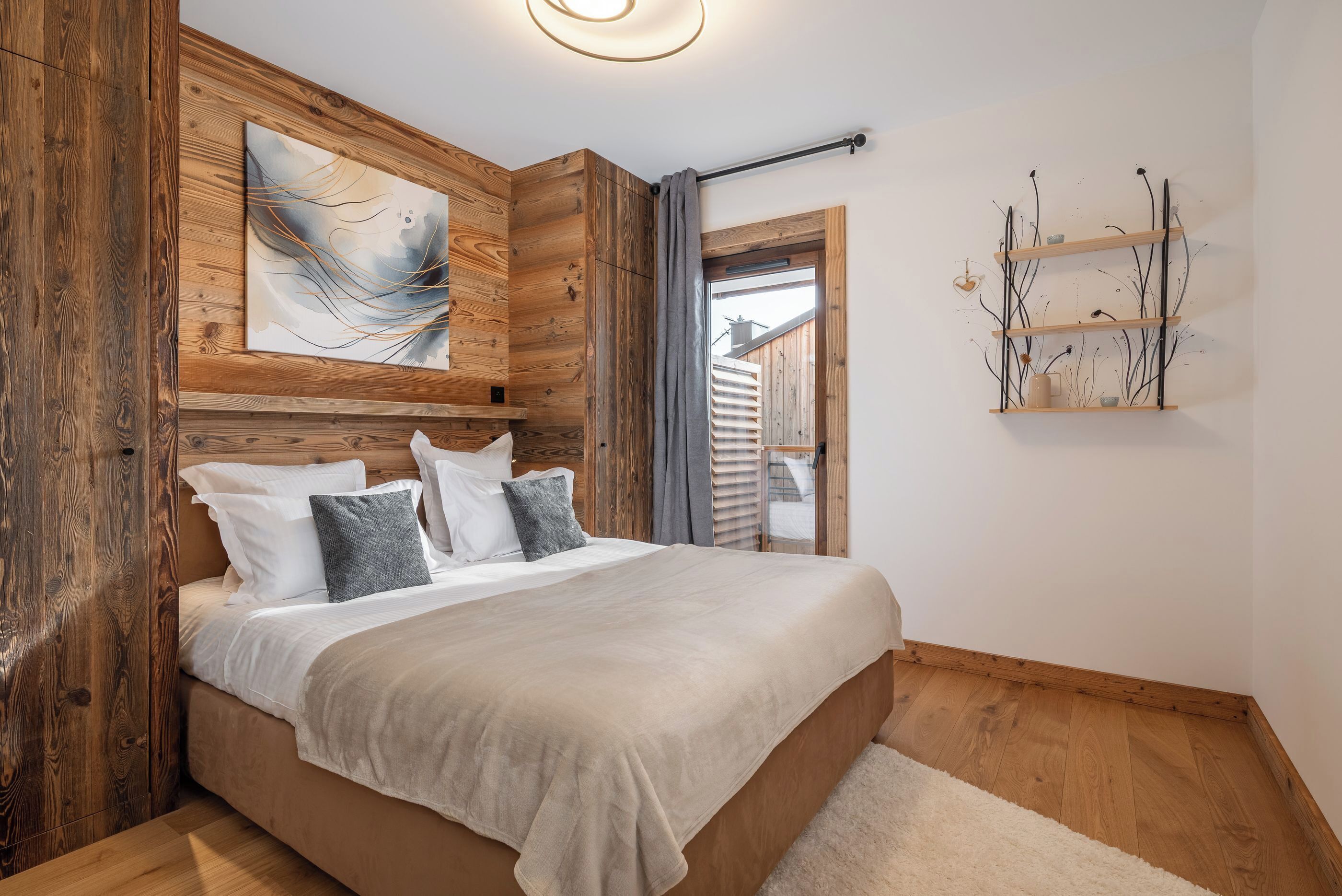 A bedroom with a wooden headboard, a large abstract painting, a bedside shelf with decorative items, and a view through an open door.