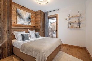 A bedroom with a wooden headboard, a large abstract painting, a bedside shelf with decorative items, and a view through an open door. - Taiga – Central Apartment Near Slopes, Huez (Huez)