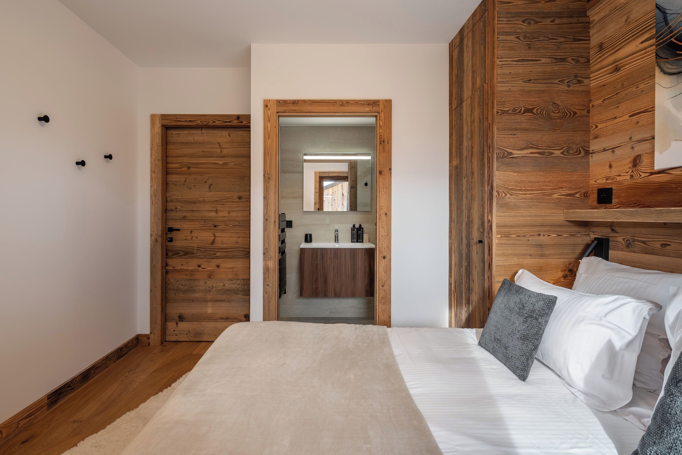 A bedroom with a wooden headboard, a large bed with white bedding, and a view into the bathroom through a doorway.