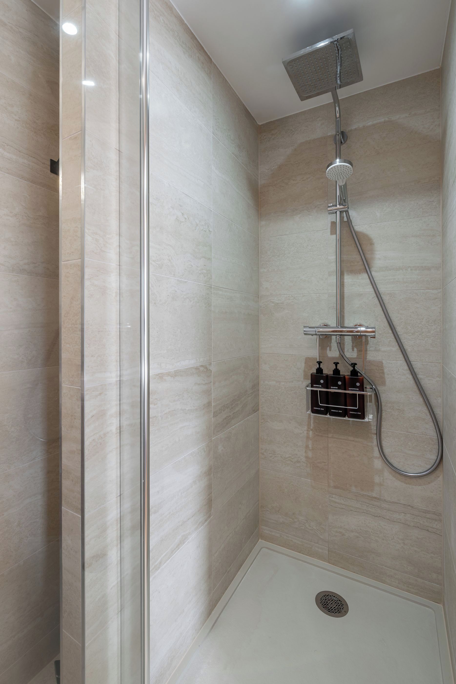 Una ducha moderna con cabina de vidrio, cabezal de ducha de mano y dispensador de jabón integrado.