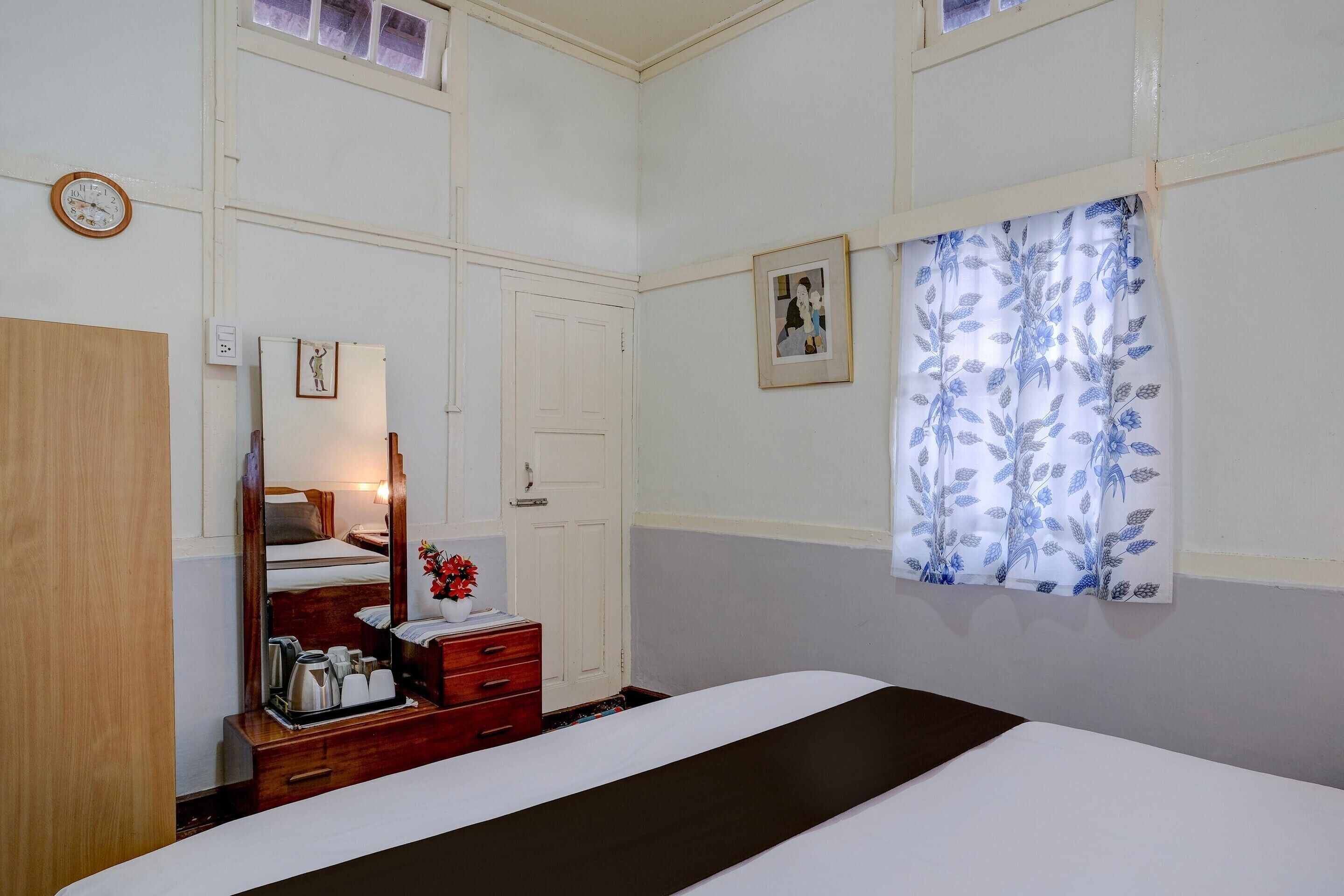 Habitación de hotel con cama, cómoda, espejo, puerta y ventana con cortinas florales.