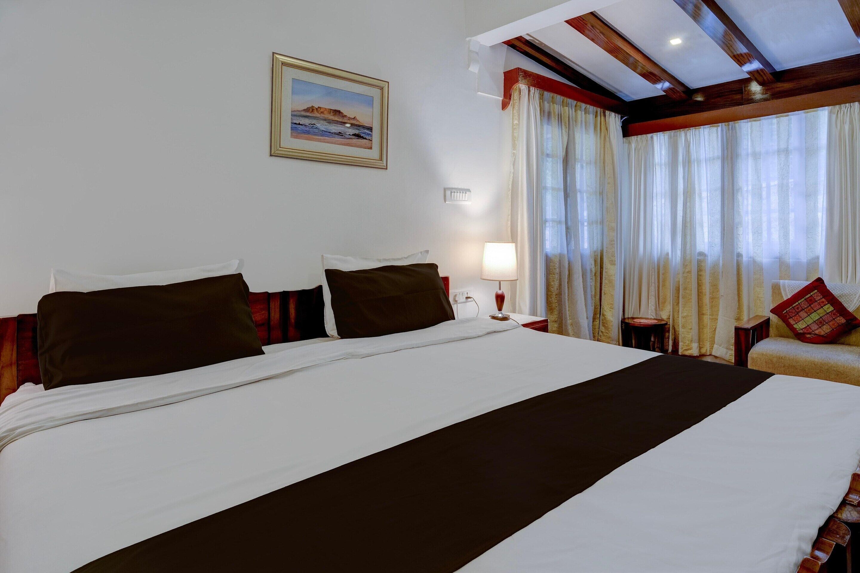 A hotel room with a large bed, a nightstand, a lamp, a chair, and a painting on the wall.