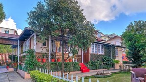 Um edifício residencial com um jardim frontal, uma cerca branca de piquete e uma escadaria vermelha que leva à entrada.
