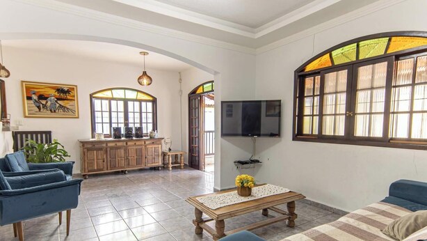 Uma sala de estar ampla com TV, sofás, mesa de centro e área de cozinha com armário e TV.