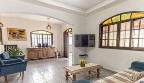 Una sala de estar amplia con televisor, sofás, una mesa de centro y una zona de cocina con un armario y televisor.