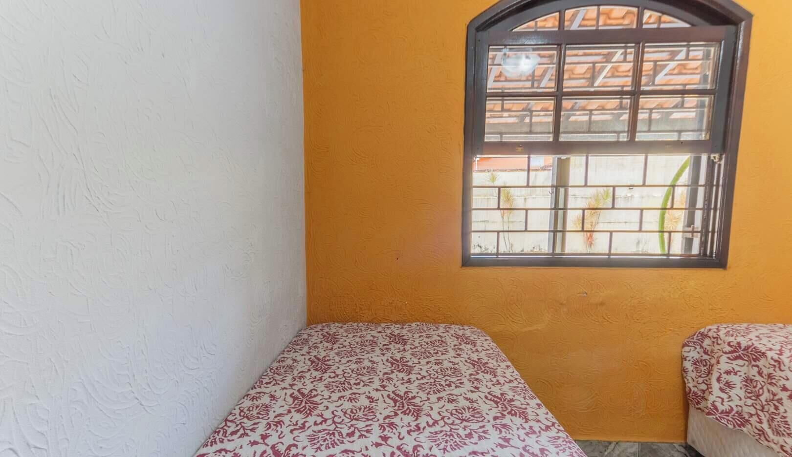 A small room with two beds, a window with bars, and a yellow wall.