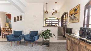 Um hall com duas cadeiras azuis, uma planta em vaso, um armário de madeira e um quadro na parede.
