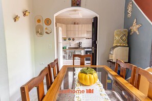 Un coin repas avec une table dressée pour deux personnes, une cuisine en arrière-plan et des œuvres d’art décoratives accrochées au mur.