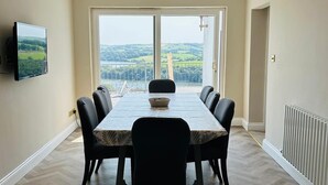 Une salle à manger avec une grande table, des chaises, un téléviseur et une vue sur l’extérieur.