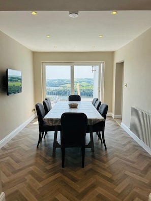 Un comedor con una mesa grande, sillas, un televisor y vistas al exterior.