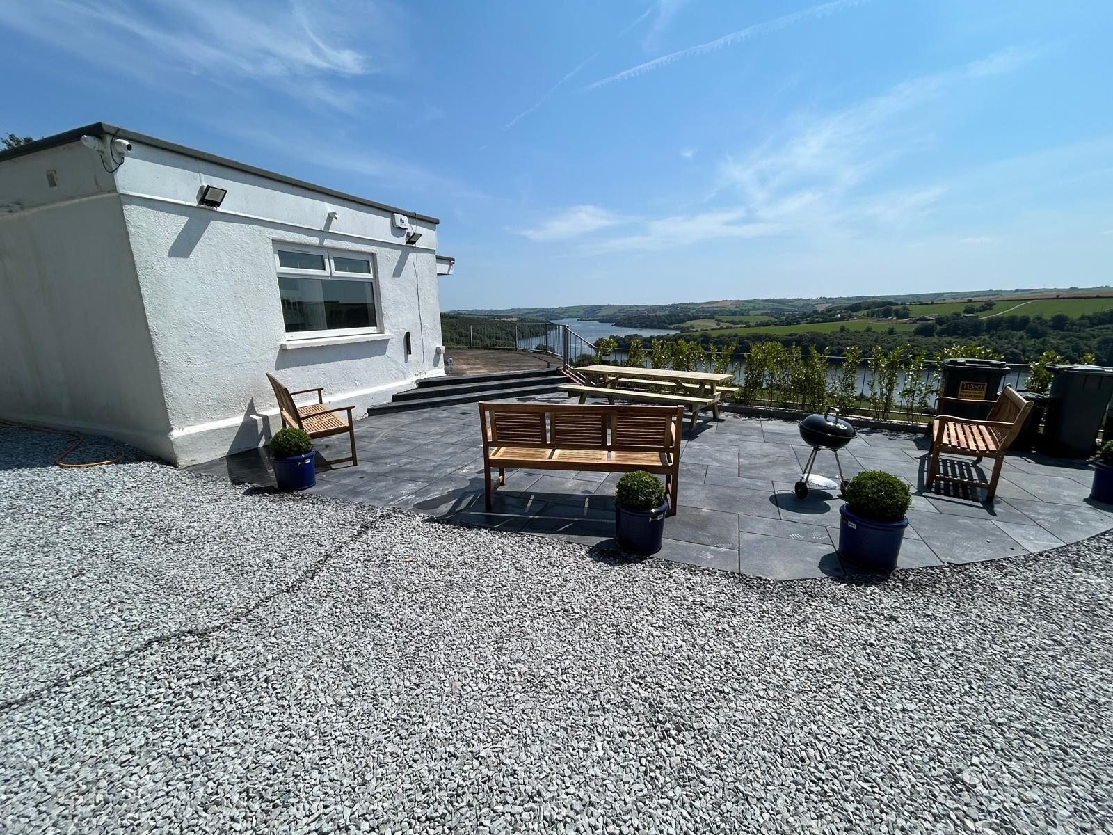 A rooftop terrace with outdoor seating, a view of the countryside, and a building with a white exterior.