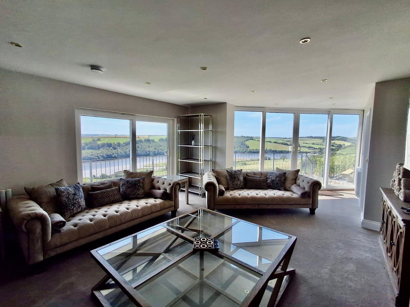 A spacious living room with two sofas, a glass coffee table, and large windows offering a scenic view.