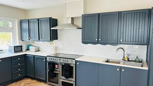 Une cuisine moderne avec des meubles de couleur bleu foncé, une cuisinière en acier inoxydable et un parquet en bois disposé en chevrons.