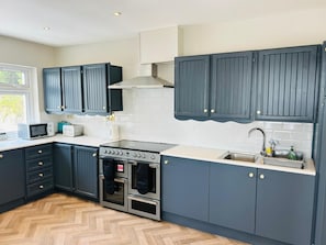Una cocina moderna con armarios azul oscuro, una estufa de acero inoxidable y un piso de madera en patrón de espiga.