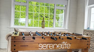 A foosball table with the brand 'serenelife' in a room with a herringbone floor and a window with a view of greenery.