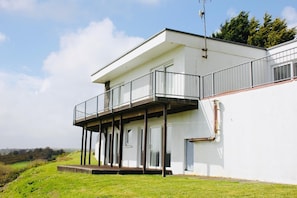 A modern two-story building with a balcony, white exterior walls, and a flat roof.