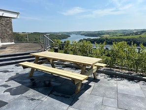 Una mesa de picnic de madera en un patio de piedra con vistas a un lago y colinas.