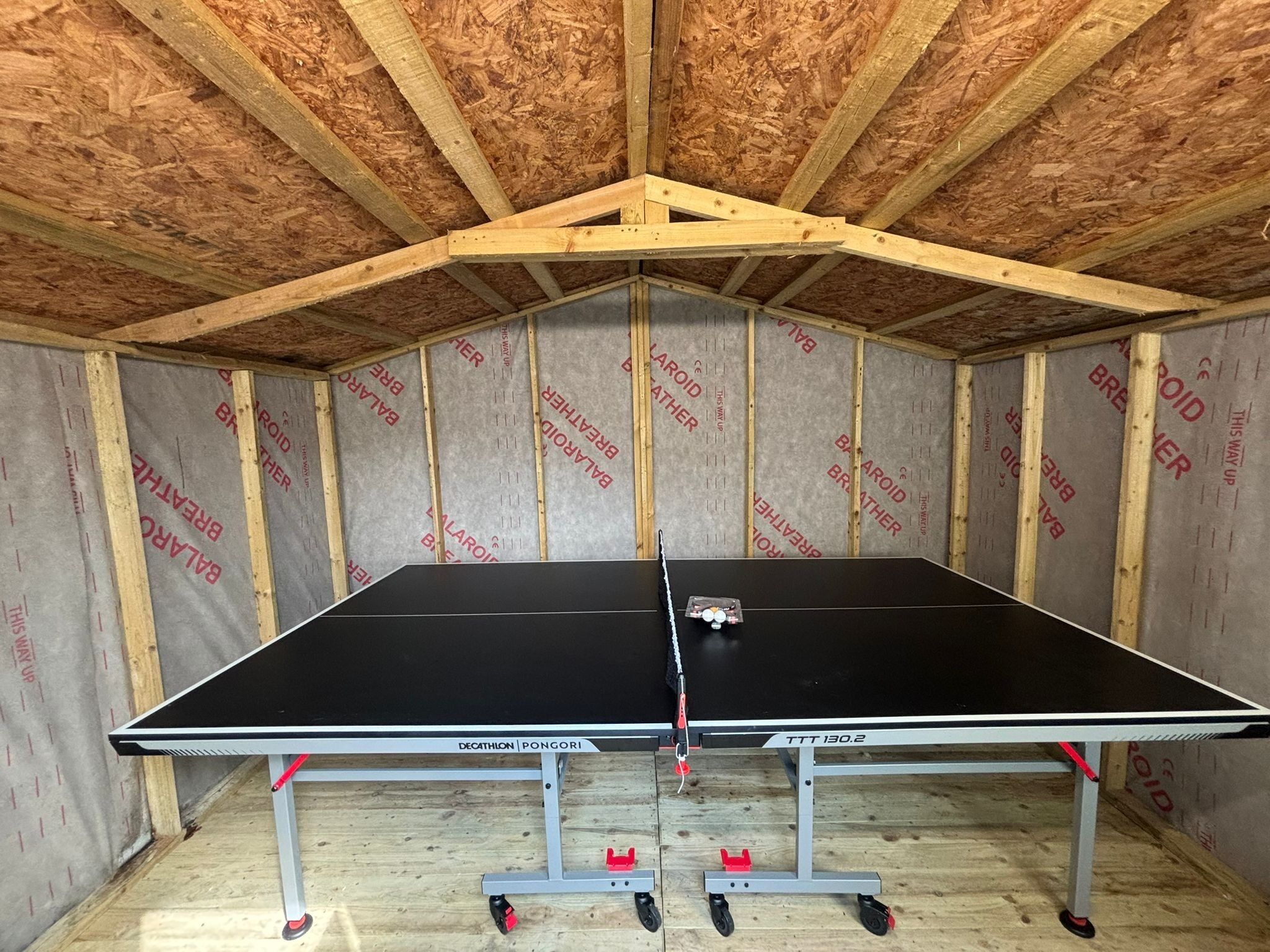 A ping pong table in a room with wooden framing and insulation.